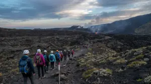Gruppo di escursionisti con casco su sentiero lavico dell’Etna, con crateri fumanti sullo sfondo