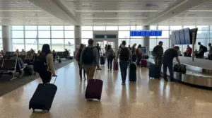 Viaggiatori in aeroporto con trolley e zaini, tra area d’imbarco e ritiro bagagli
