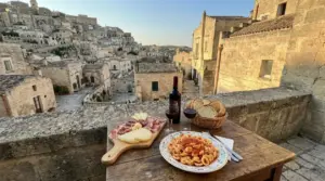 Tavolo con pasta, salumi, formaggi e vino affacciato sui Sassi di Matera al tramonto