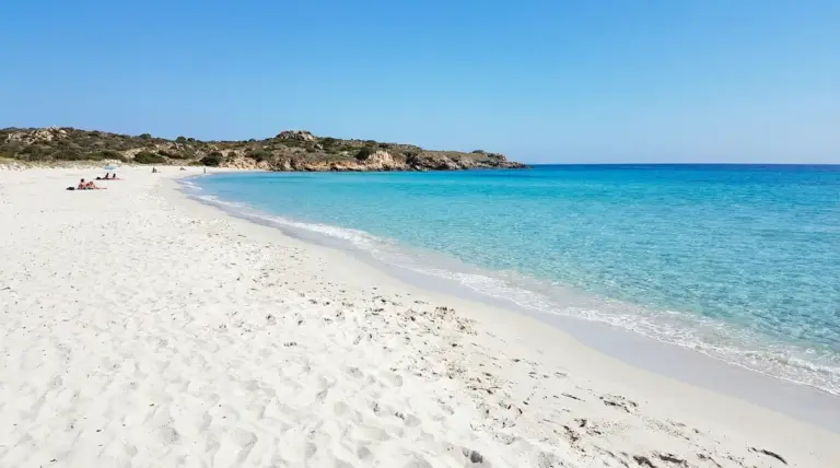 Spiaggia italiana con sabbia bianca e mare turchese, con poche persone sulla riva sotto un cielo sereno