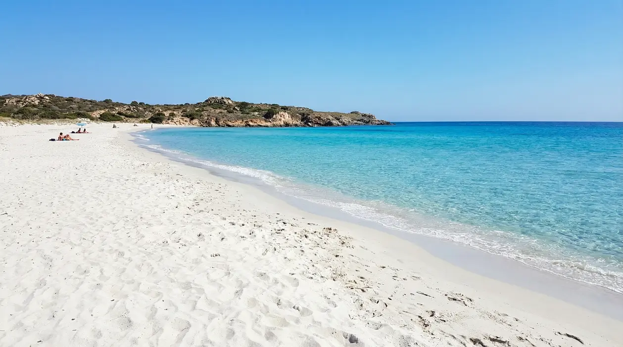 Spiaggia italiana con sabbia bianca e mare turchese, con poche persone sulla riva sotto un cielo sereno