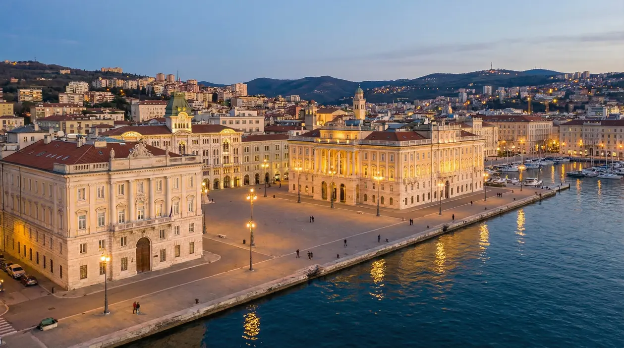 Vista serale del centro di Trieste sul mare, con piazza e palazzi storici illuminati