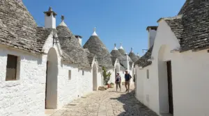 Stradina tra i trulli di Alberobello con case bianche in pietra e due visitatori a piedi