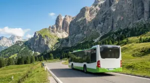 Autobus di linea su strada panoramica nelle Dolomiti, tra prati alpini e grandi pareti rocciose