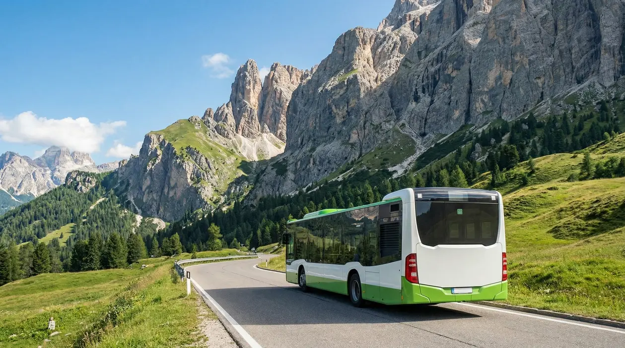 Autobus di linea su strada panoramica nelle Dolomiti, tra prati alpini e grandi pareti rocciose
